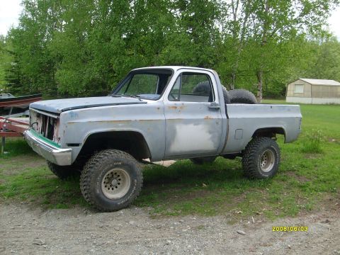 1984 Chevrolet Blazer - This lifted pickup truck appears to be from the 1970s, with a missing grille and a spare tire in the bed.