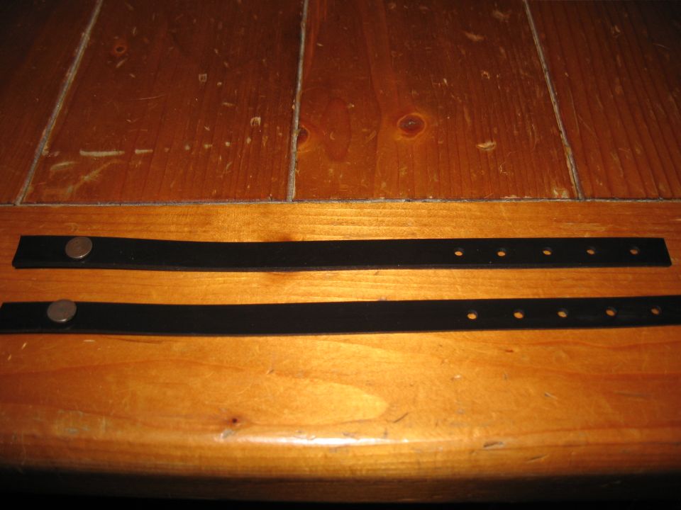 two black straps with metal snaps and holes on a wooden surface