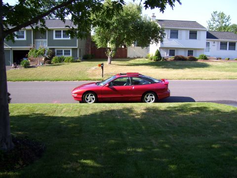 1995 Ford Probe - A red coupe is parked on the street in front of suburban houses.