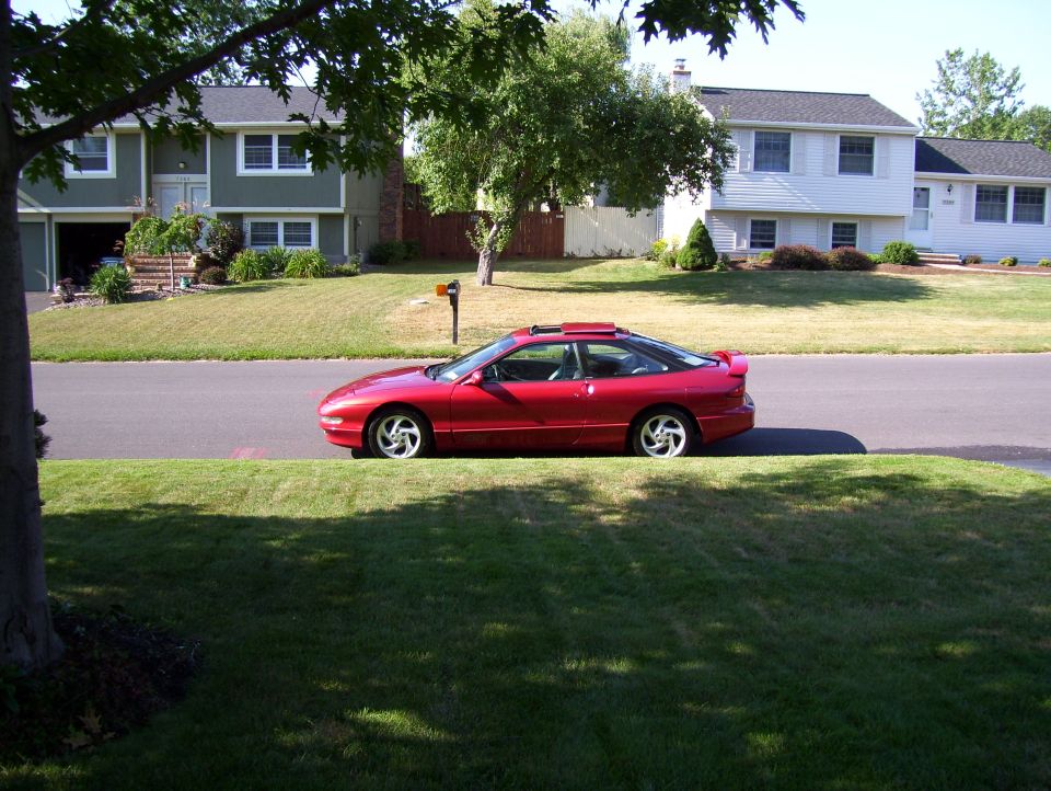 Red coupe parked on street, side view. Sunroof and spoiler visible