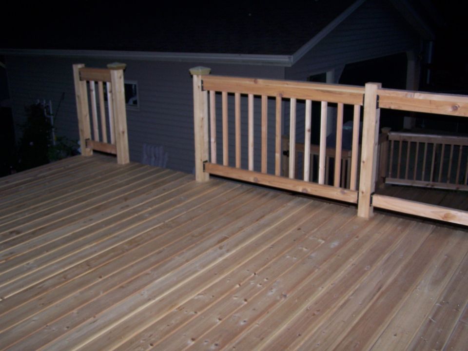 Wooden deck with railings in front of a house at night. Supermotors.net logo in corner
