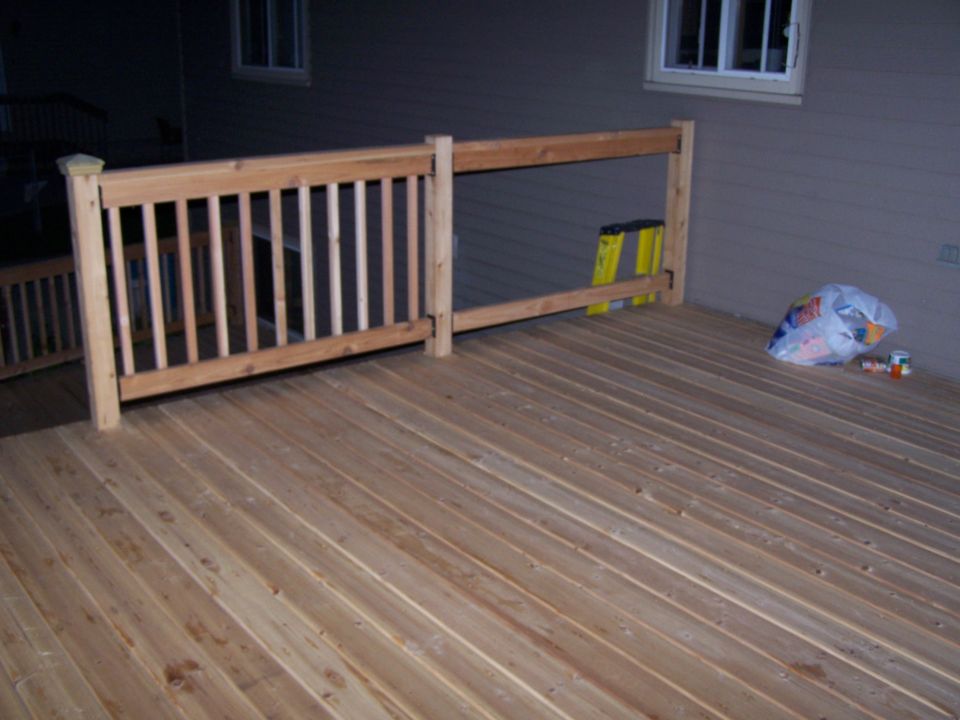Wooden deck with railing, ladder, and trash bag