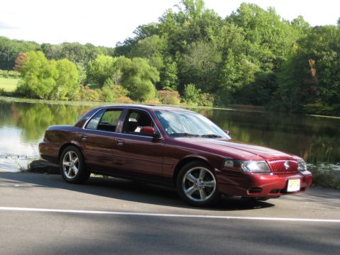 1988 Mercury Grand Marquis - Maroon sedan with aftermarket wheels parked beside a lake with trees in the background.