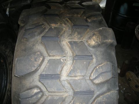 1979 Ford Bronco - A close-up, low-angle shot of the tread pattern on a large, worn tire, likely for an off-road vehicle. The tire is dark gray and appears to…