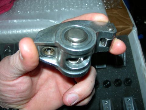 1984 Ford Bronco - A hand holds a metal engine component, likely a rocker arm, with a roller tip. The component is silver and appears to be part of an engine…