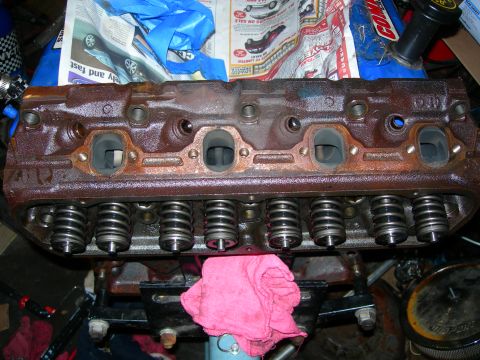 1984 Ford Bronco - A heavily rusted engine cylinder head with visible valve springs and ports is shown in a workshop setting. The cylinder head is resting on…