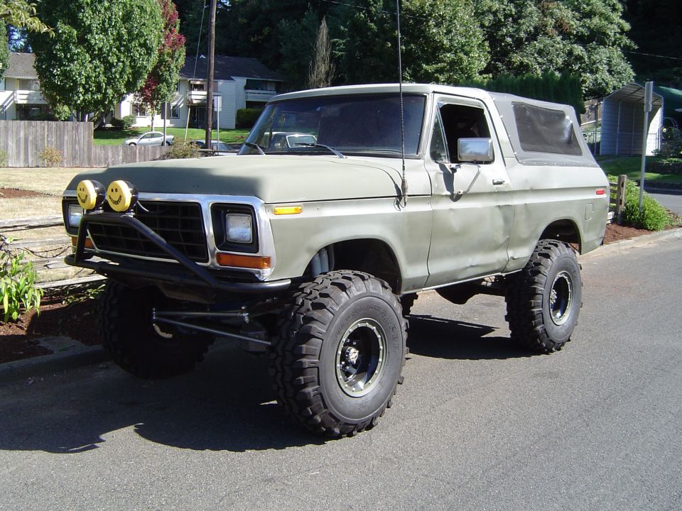 1978 Ford Bronco lifted with off-road tires and custom bumper, parked on a street.