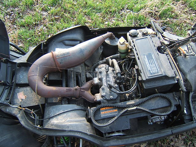 Snowmobile two-stroke engine bay with rusty expansion chamber and drive belt