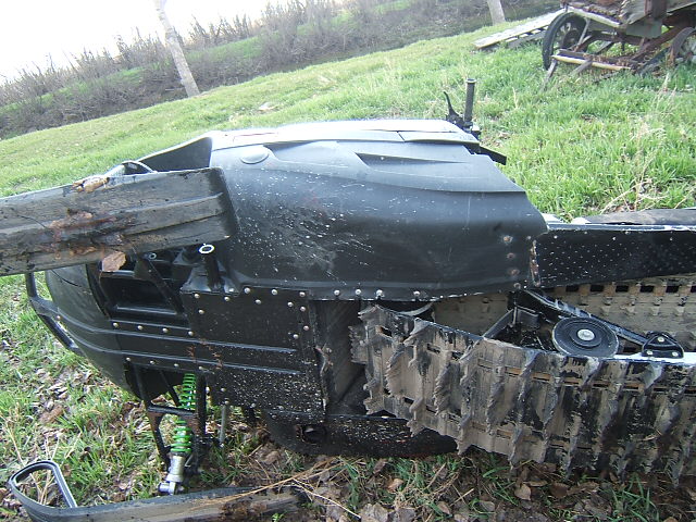Black snowmobile on its side in grass with exposed track and green shock