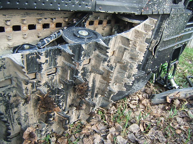Close-up of snowmobile paddle track and idler wheel caked with mud and leaves