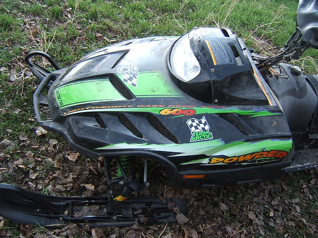 Green and black Arctic Cat Powder 600 snowmobile lying on leaf-covered ground