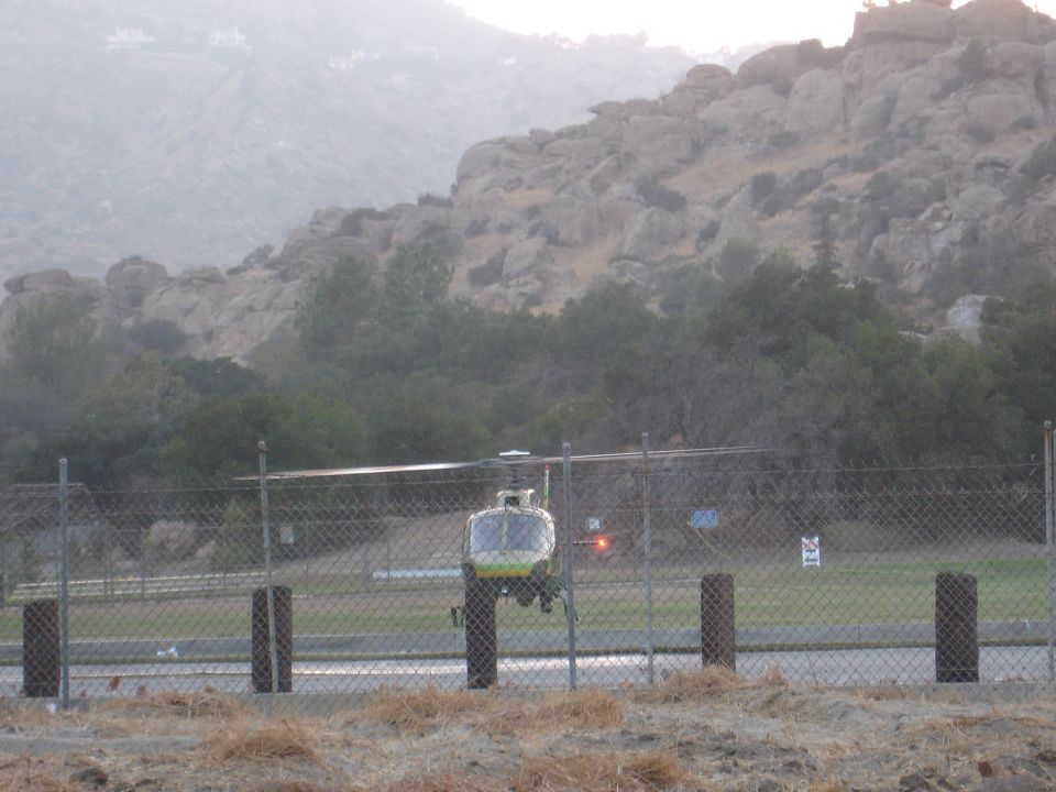 Helicopter hovering near a fence with a rocky hillside.
