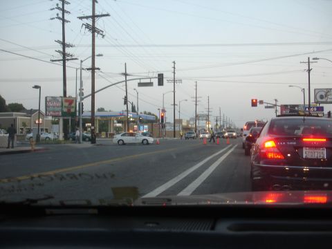 1993 Ford Taurus - A busy street scene with multiple cars in traffic, a gas station, and traffic cones indicating some form of road work or event.