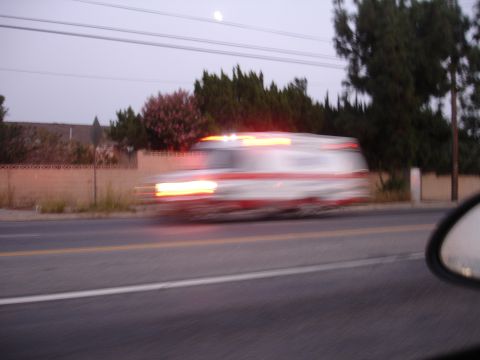 1993 Ford Taurus - Motion-blurred ambulance with red and white markings travels down a road at dusk.