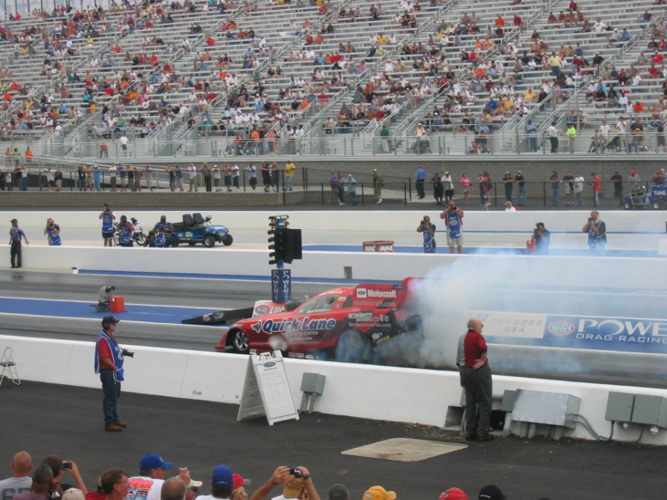 Red drag racing car with 'Quick Lane' livery emitting smoke on a track