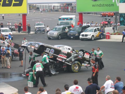 1992 Ford Mustang - A team services a dragster at a racing event, with several support vehicles and spectators present.