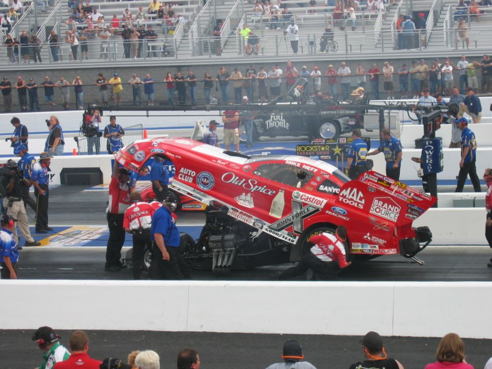 Red Old Spice drag car with "Mike Neff" and "John Force Racing" text, being serviced by crew