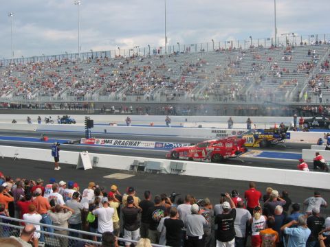 1992 Ford Mustang - Two drag racing cars compete on a track with a large crowd in the stands.