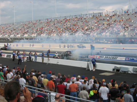 1992 Ford Mustang - A drag race is underway with cars and motorcycles on the track, while spectators fill the grandstands and line the fence.