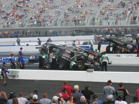 1992 Ford Mustang - Drag racing cars and their crews are seen on the track during an event, with spectators in the background.