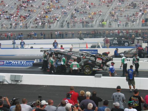 1992 Ford Mustang - A drag racing car is being tended to by its crew on the track, with a crowd watching from the stands.