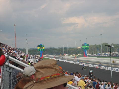 1992 Ford Mustang - A drag racing event is underway with spectators watching from the stands as vehicles compete on the track under a cloudy sky.