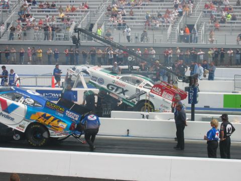 1992 Ford Mustang - Two drag racing cars are being attended to by crew members on a race track with spectators in the background.