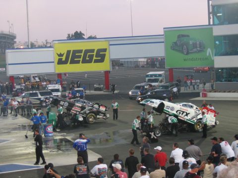 1992 Ford Mustang - NHRA drag racing cars are serviced by their crews on the track under large sponsor signs.