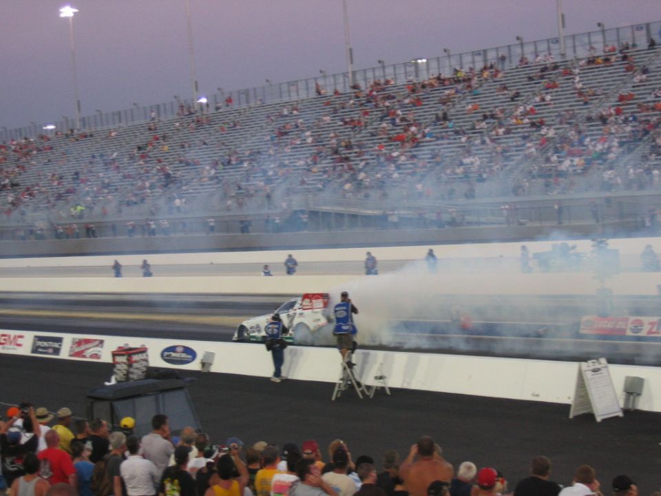 drag car doing a burnout on a track with spectators in bleachers