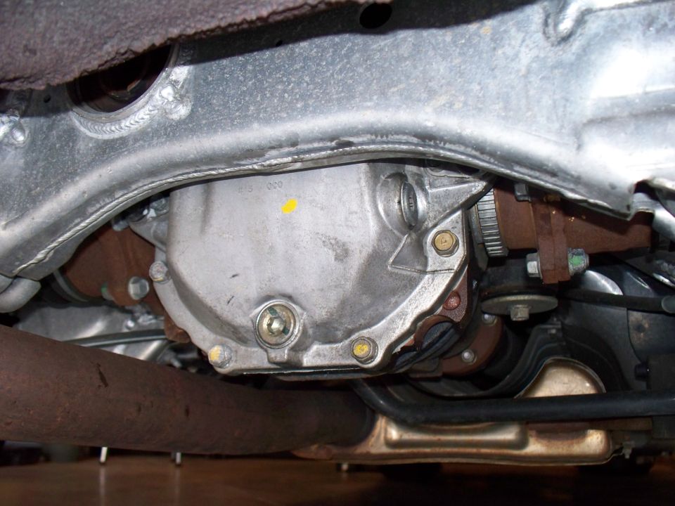Underside view of aluminum rear differential with subframe and rusty exhaust pipe