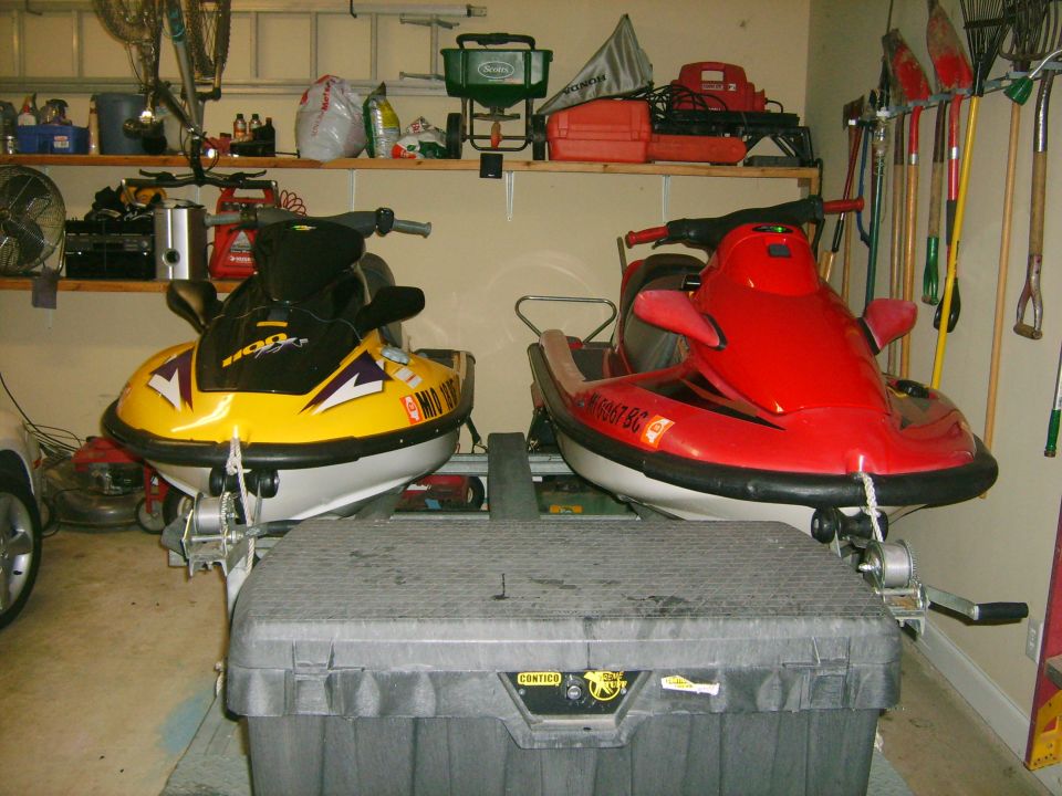 Two jet skis, one yellow and one red, parked in a garage