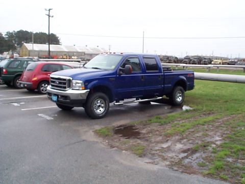 1978 Ford Bronco - A blue Ford F-250 Super Duty pickup truck is parked in a lot next to other vehicles on a cloudy day.