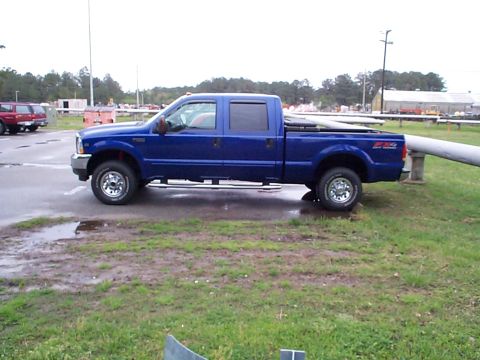 1978 Ford Bronco - A blue Ford F-250 Super Duty pickup truck is parked on a wet surface next to a grassy area.