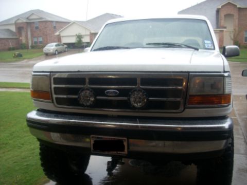 1992 Ford Bronco - Head-on view of a white Ford truck with the 1992-96 aero front end, chrome bumper and grille bar with a blue Ford oval, and a pair of round…
