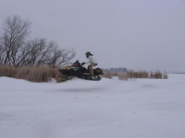Rider on a black snowmobile jumping over a snowfield under gray sky