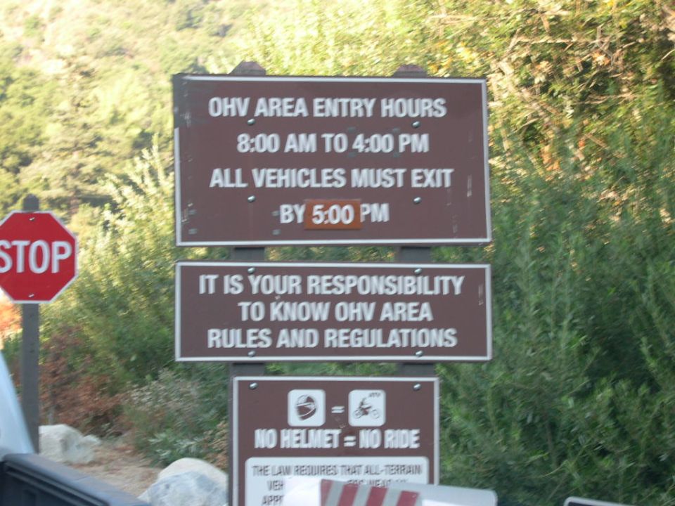 Brown OHV area regulation signs near a stop sign on a wooded road