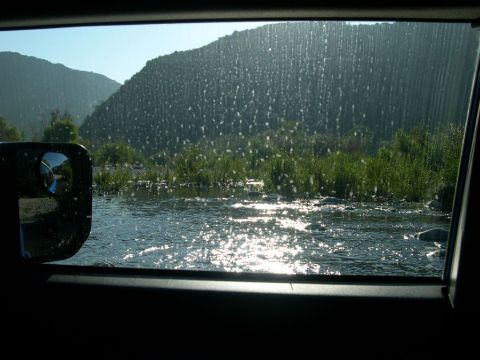 2007 Toyota FJ Cruiser - Sunlight sparkles on the water during a river crossing, with a mountain covered in white specks in the distance.