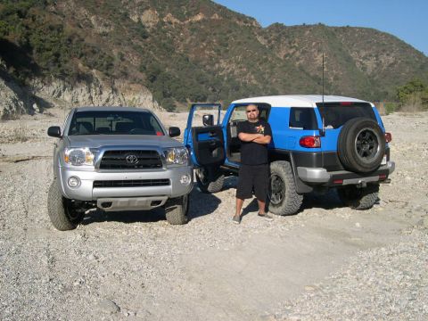 2007 Toyota FJ Cruiser - A silver Toyota Tacoma and a blue 2007 Toyota FJ Cruiser are parked in a rocky, dry riverbed with mountains in the background.
