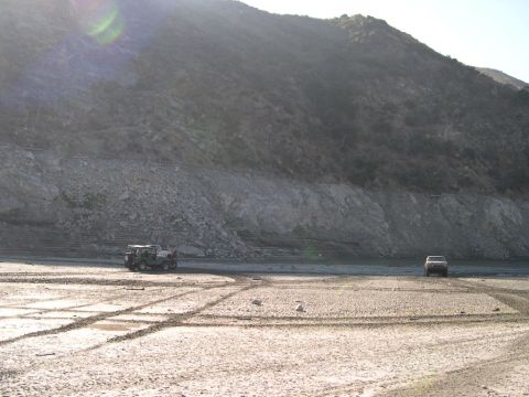 2007 Toyota FJ Cruiser - Two off-road vehicles traverse a barren, dry landscape under a large, rocky hill.