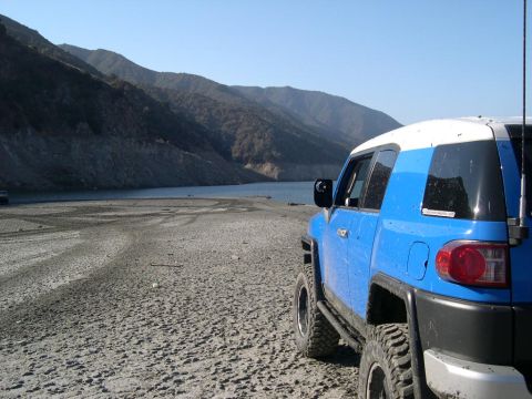 2007 Toyota FJ Cruiser - A blue 2007 Toyota FJ Cruiser sits parked on a dry lake bed with mountains in the background.
