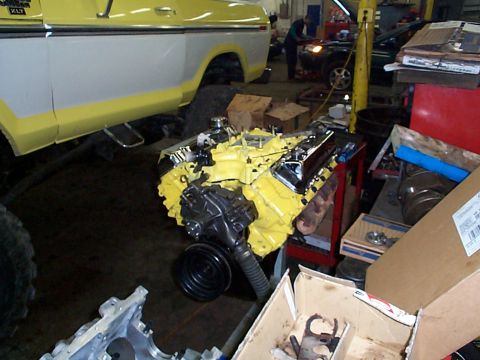 1978 Ford Bronco - A yellow engine is ready for installation in a workshop, with a truck and another vehicle visible.
