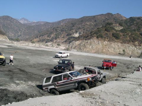 2007 Toyota FJ Cruiser - Several off-road vehicles navigate a challenging terrain in a dry riverbed, with mountains looming in the distance.