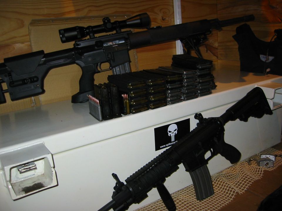 Two black rifles and ammunition magazines on a white surface with a skull sticker.