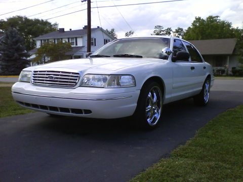2003 Ford Crown Victoria - A white 2003 Ford Crown Victoria is parked on a driveway with chrome wheels. The sedan is viewed from a low angle, showing its front quarte…
