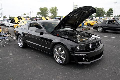 2007 Ford Mustang - A black 2007 Ford Mustang GT coupe is parked in an asphalt lot with its hood open, showcasing the engine. The car has chrome wheels and is…