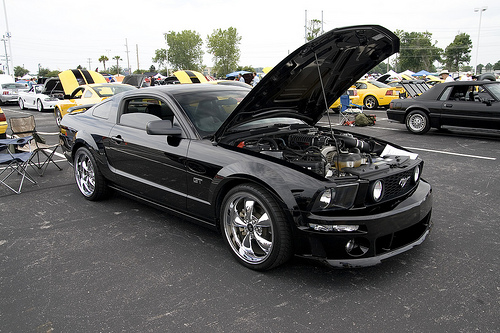 Black 2007 Ford Mustang GT with hood open, chrome wheels, at an outdoor car show.