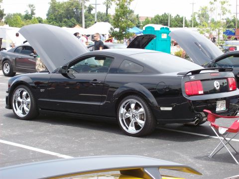 2007 Ford Mustang - A black 2007 Ford Mustang GT coupe is parked in a lot with its hood open. The car has chrome wheels and a spoiler, and a red folding chair…