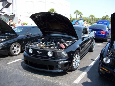 2007 Ford Mustang - A black Ford Mustang with its hood open is parked in a lot, showcasing its engine and supercharger. Another black Mustang is parked to its…