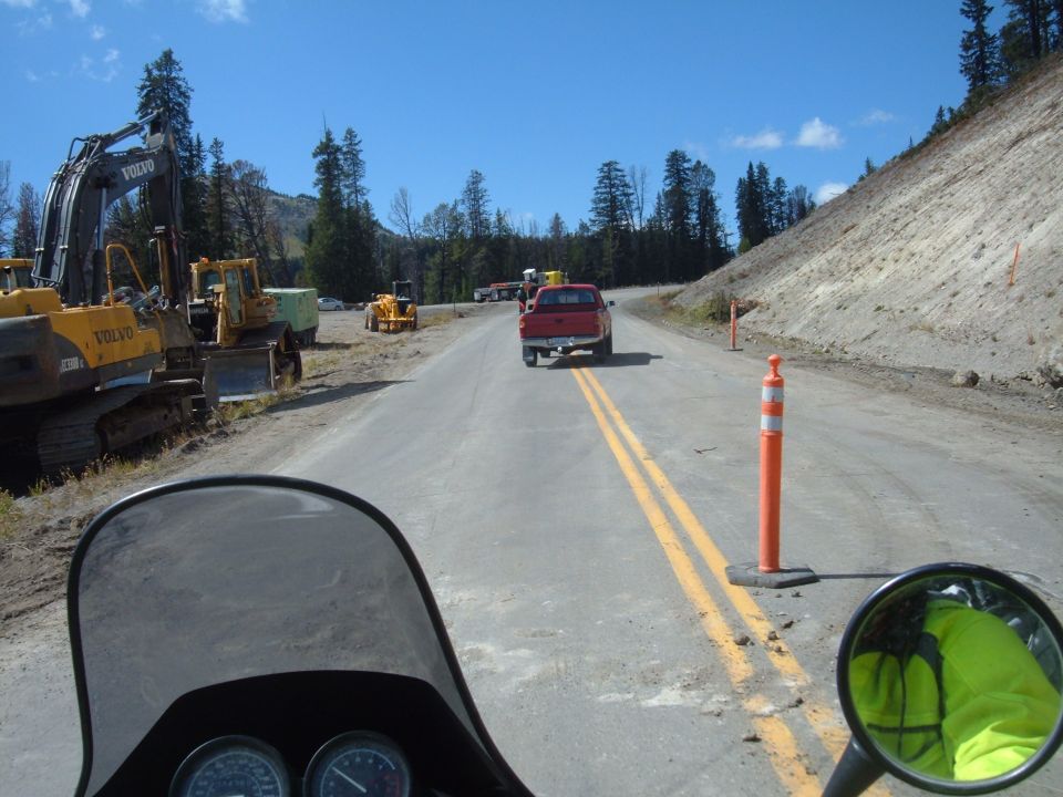 Motorcycle windshield view on a road with construction equipment and a steep hillside.