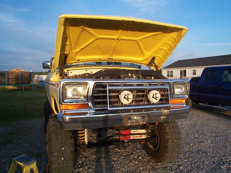 Front of yellow lifted Ford truck with hood up, chrome grille guard and twin off-road lights